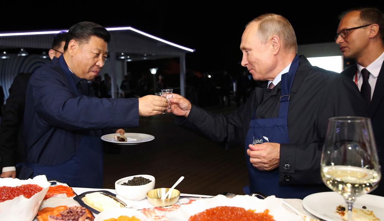 Presiden Rusia Vladimir Putin (kanan) dan Presiden China Xi Jinping (kiri) bersulang vodka saat menyantap pancake buatan bersama di sela acara Eastern Economic Forum di Vladivostok, Rusia, Selasa (11/9). (Sergei Bobylev/TASS News Agency Pool Photo via AP)