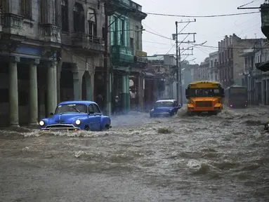 Mobil dan bus tua Amerika Serikat melewati jalan yang banjir di Havana, Kuba, 30 Juni 2021. Hujan deras dan selokan yang tidak berfungsi menyebabkan banjir di jalan-jalan di Havana. (YAMIL LAGE/AFP)