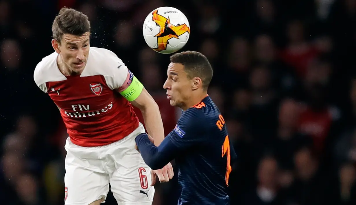 Kapten Arsenal, Laurent Koscielny berebut bola dengan pemain Valencia, Rodrigo dalam leg pertama semifinal Liga Europa di Emirates Stadium, Jumat (3/5/2019). Sempat tertinggal, Arsenal berhasil mengalahkan tamunya, Valencia dengan skor 3-1. (AP/Kirsty Wigglesworth)
