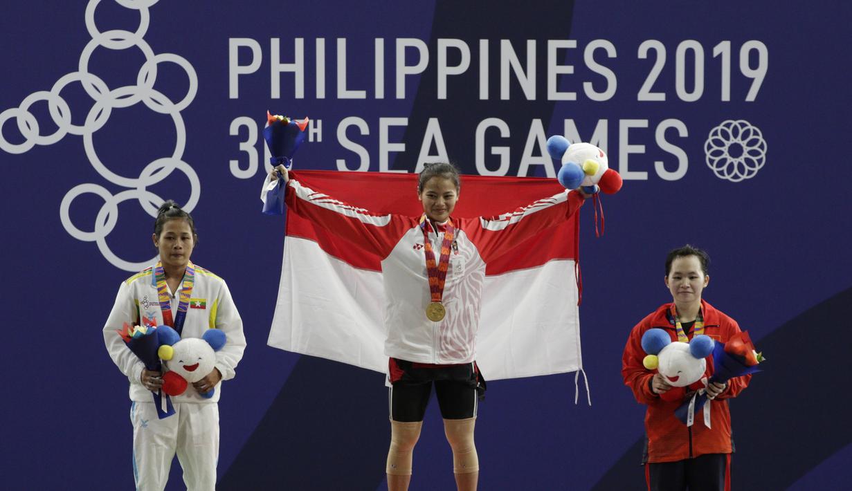Lifter Aisyah Windy mengibarkan bendera saat naik podium usai mendapatkan medali emas SEA Games 2019 cabang angkat besi nomor 49 kg di Stadion Rizal Memorial, Manila, Minggu (1/12). Dirinya meraih emas dengan total angkatan 104 kg. (Bola.com/M Iqbal Ichsa