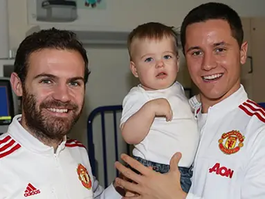 Pemain Manchester United, Ander Herrera, menggendong seorang anak yang sedang sakit saat mengunjungi Rumah Sakit Royal Manchester Children bersama rekan setimnya, Juan Mata. (www.manutd.com)