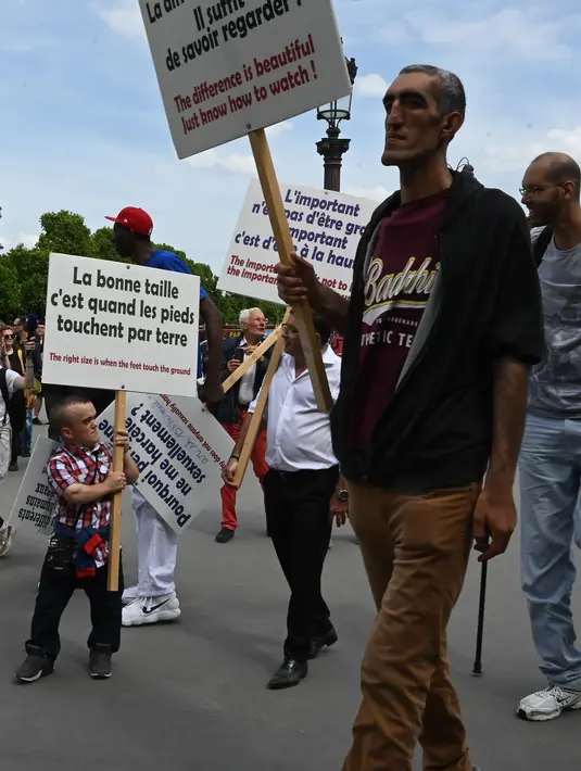 Sejumlah pria bertubuh tinggi berjalan sambil membawa poster saat melakukan pertemuan di Champs-Elysees Avenue di Paris, Prancis (14/6/2019). Kemunculan mereka di Champs-Elysees Avenue sampai mengundang perhatian warga dan penyiar televisi. (AFP Photo/Dominique Faget)
