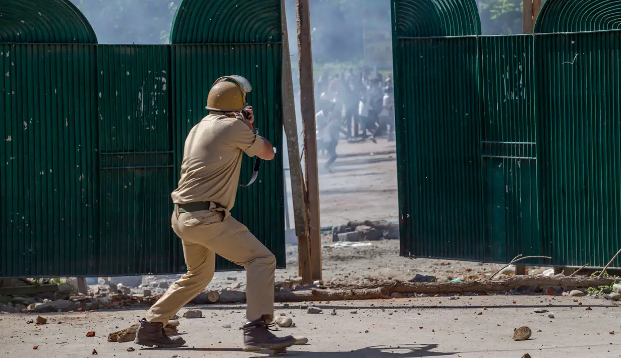 Polisi India bersiap menembakkan bom gas air mata ke arah mahasiswa Kashmir yang terlihat di gerbang kampus mereka di Srinagar, Kashmir yang dikuasai India, (23/5). (AP Photo/Dar Yasin) 