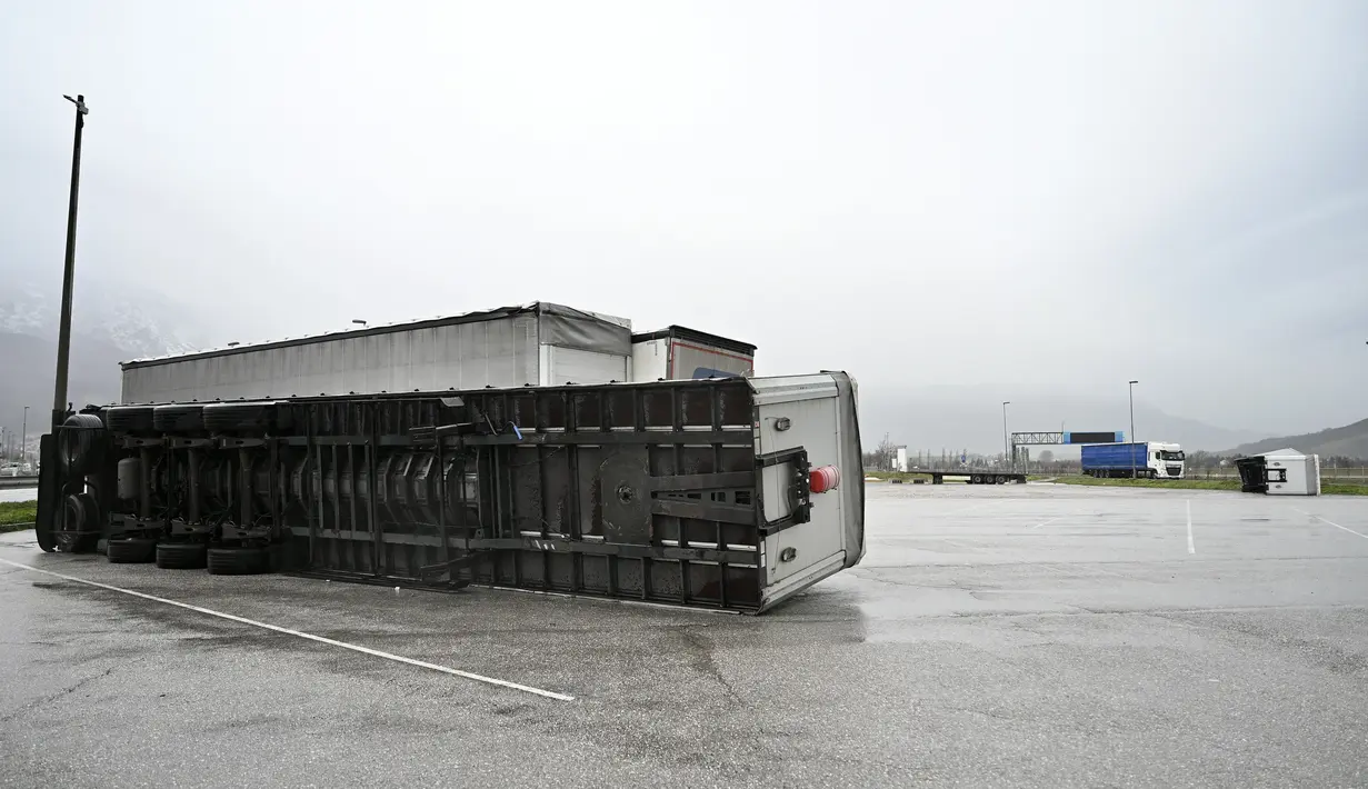 Truk trailer terbalik tergeletak di tempat parkir truk di Ajdovscina, Slovenia, saat angin bora bertiup dengan hembusan hingga 140 km/jam pada Senin (23/1/2023). Hujan salju lebat dan angin bora yang kencang menghambat lalu lintas dan menyebabkan pemadaman listrik di seluruh Slovenia. (Jure Makovec / AFP)