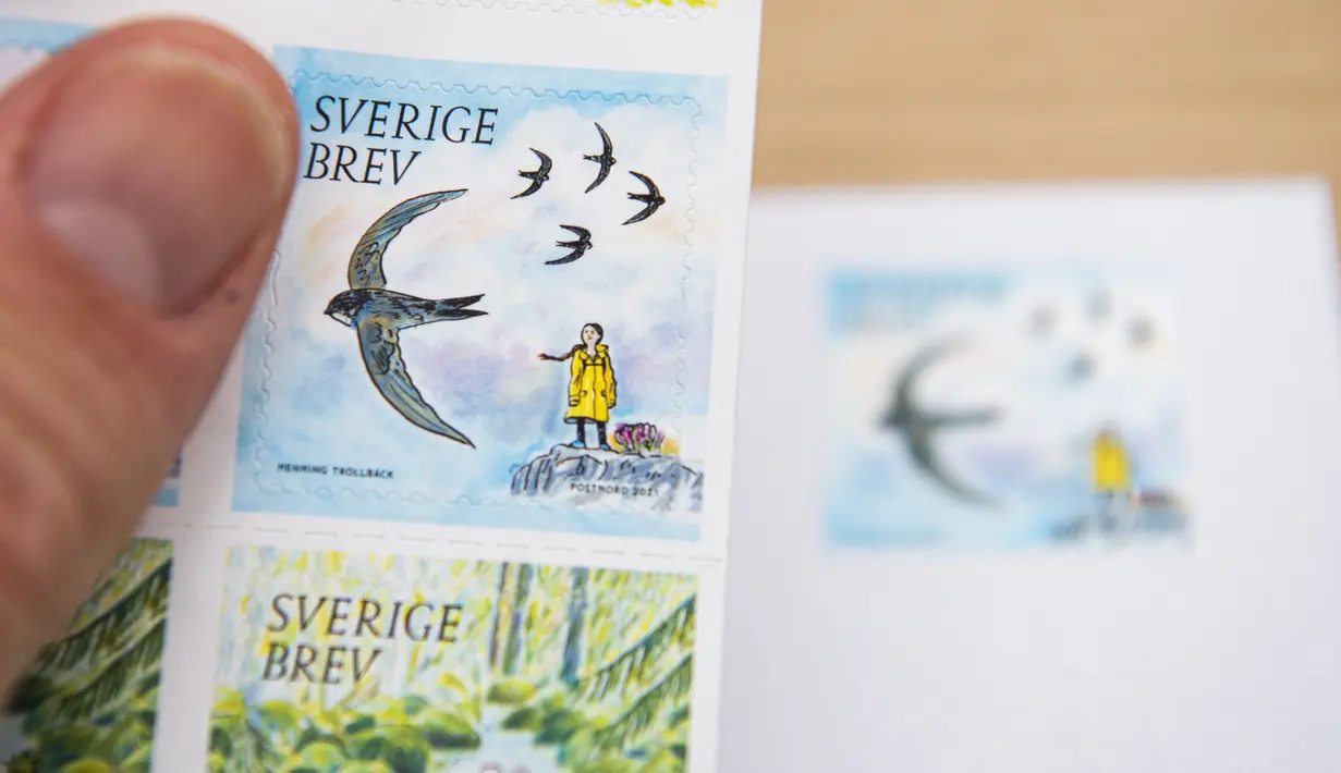 Seorang pria memegang prangko pos yang menggambarkan aktivis lingkungan remaja asal Swedia, Greta Thunberg di Stockholm pada 15 Januari 2021. Greta Thunberg ditampilkan dalam jas hujan kuning khasnya dengan kepang yang tertiup angin dan berdiri di atas bukit. (Jonathan NACKSTRAND/AFP)