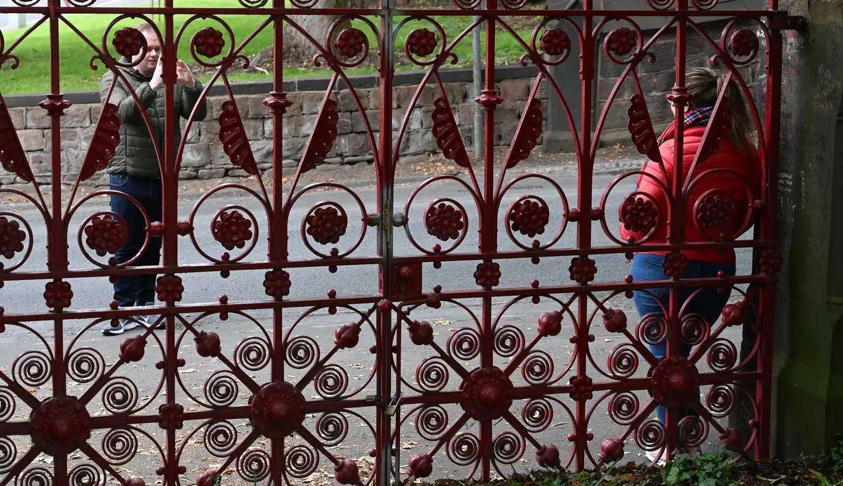 Pengunjung berpose di depan gerbang  Strawberry Fields yang baru dibuka untuk umum di Liverpool, Rabu (18/9/2019). Strawberry Field menjadi salah satu tempat ikonis ketika John Lennon menulis lagu The Beatles “Strawberry Fields Forever” dalam album Sgt.pepper Lonely Hearts Club Band (Paul ELLIS/AFP)