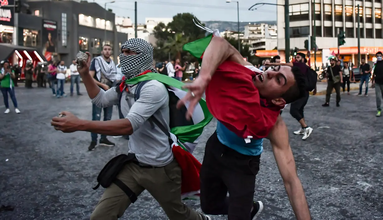 Aksi melempar batu para demonstran ke kedutaan Israel di Athena, Yunani, Selasa (15/5). Mereka mengecam tindakan tentara Israel menembak mati puluhan warga Palestina di perbatasan Gaza yang berunjuk rasa menentang pembukaan kedubes AS (AFP/Aris MESSINIS)