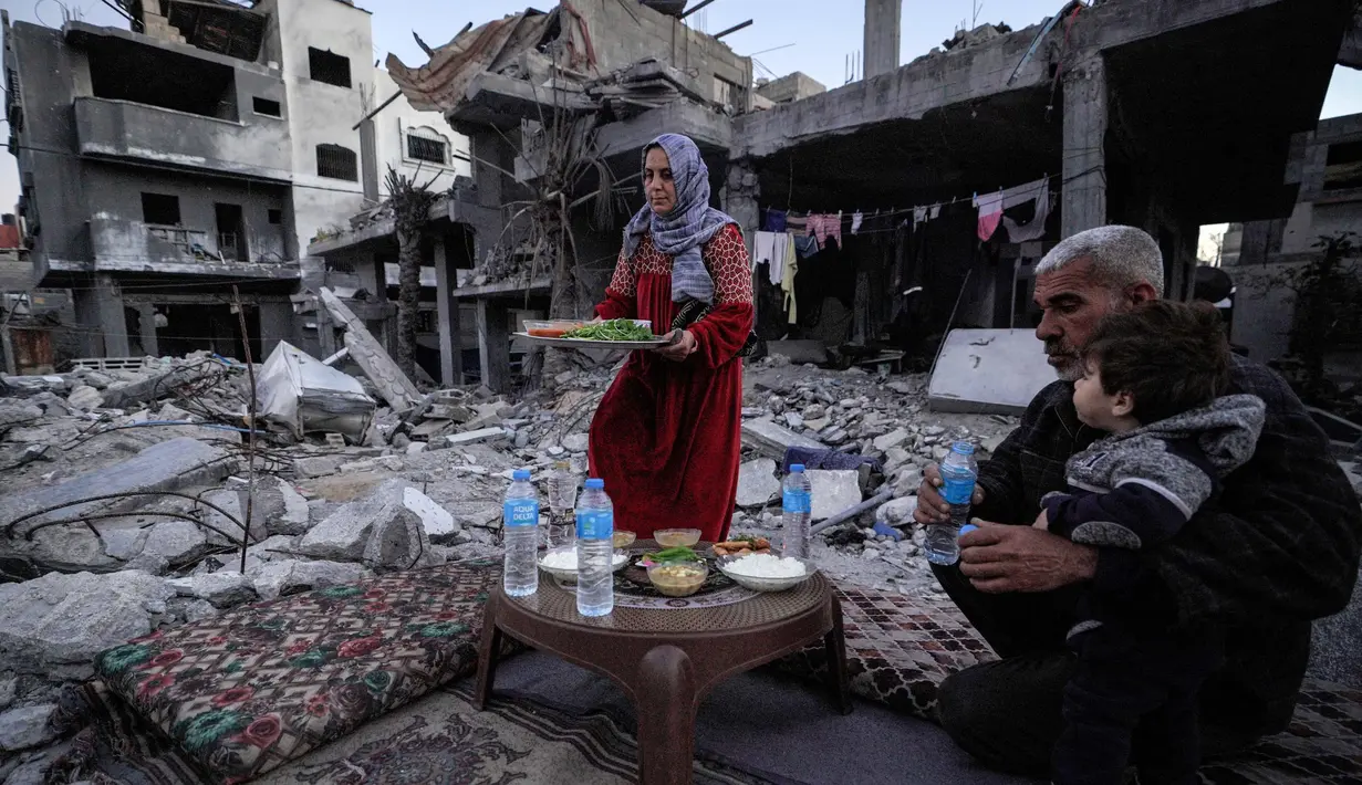Keluarga Al-Naji dari Palestina menyantap hidangan berbuka puasa, di tengah reruntuhan rumah keluarga mereka, pada hari pertama bulan puasa Ramadan, di Deir el-Balah di Jalur Gaza tengah pada 11 Maret 2024. (Foto: AFP)