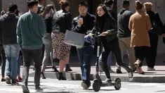 Seorang wanita menyebrang jalanan mengendarai skuter bermotor di San Francisco (17/4). San Francisco menghentikan operasi perusahaan yang menyewakan skuter bermotor. (AP/Jeff Chiu)