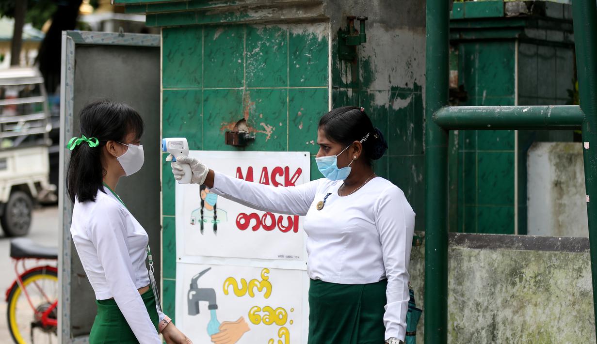 Seorang guru mengenakan masker mengukur suhu tubuh siswa di gerbang sekolah saat hari pendaftaran sekolah di Yangon, Myanmar  (13/7/2020). Myanmar sejak Selasa (7/7) memulai pendaftaran sekolah untuk tahun ajaran 2020-2021, yang tertunda akibat pandemi COVID-19. (Xinhua/U Aung)