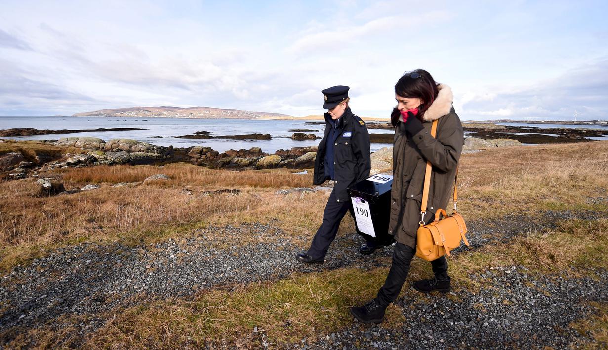 Margaret Byrne (kiri) berjalan mengawal pejabat ketua, Majella Harkin saat mendistribusikan kotak suara di Inishfree, Irlandia, Kamis (25/2). Pulau terpencil ini hanya terdapat empat orang yang memiliki hak pilih. (REUTERS/Clodagh Kilcoyne)