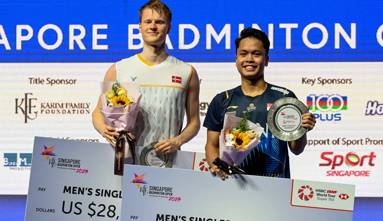 Pebulu tangkis tunggal putra Indonesia, Anthony Sinisuka Ginting (kanan) berpose dengan trofi juara Singapore Open 2023 bersama wakil Denmark, Anders Antonsen yang dikalahkannya di laga final dengan dua game langsung 21-16, 21-13 di Singapore Indoor Stadium, Singapura, Minggu (11/6/2023). (AFP/Roslan Rahman)