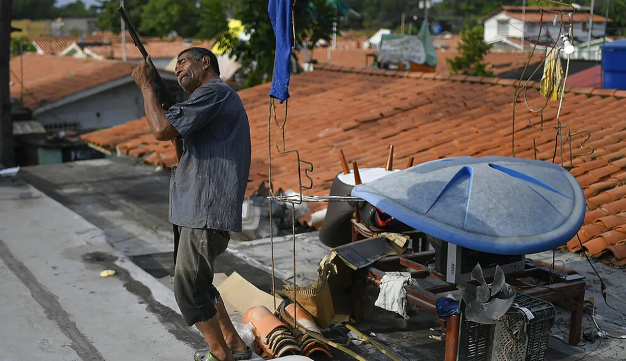 Carlos Gelez berdiri di atap rumahnya yang banjir sambil memegang senapan mainan untuk menakut-nakuti pencuri di Mata Redonda, Maracay, Venezuela, Rabu (21/10/2020). Lusinan keluarga mencari perlindungan di atap rumah mereka untuk melindungi barang pribadi mereka. (AP Photo/Matias Delacroix)