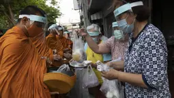 Warga menyerahkan makanan kepada para biksu Buddha yang memakai pelindung wajah untuk melindungi diri dari virus corona COVID-19 saat mengumpulkan sedekah di Bangkok, Thailand, Selasa (31/3/2020). Hingga 30 Maret 2020, jumlah kasus positif COVID-19 di Thailand ada 1.524. (AP Photo/Sakchai Lalit)