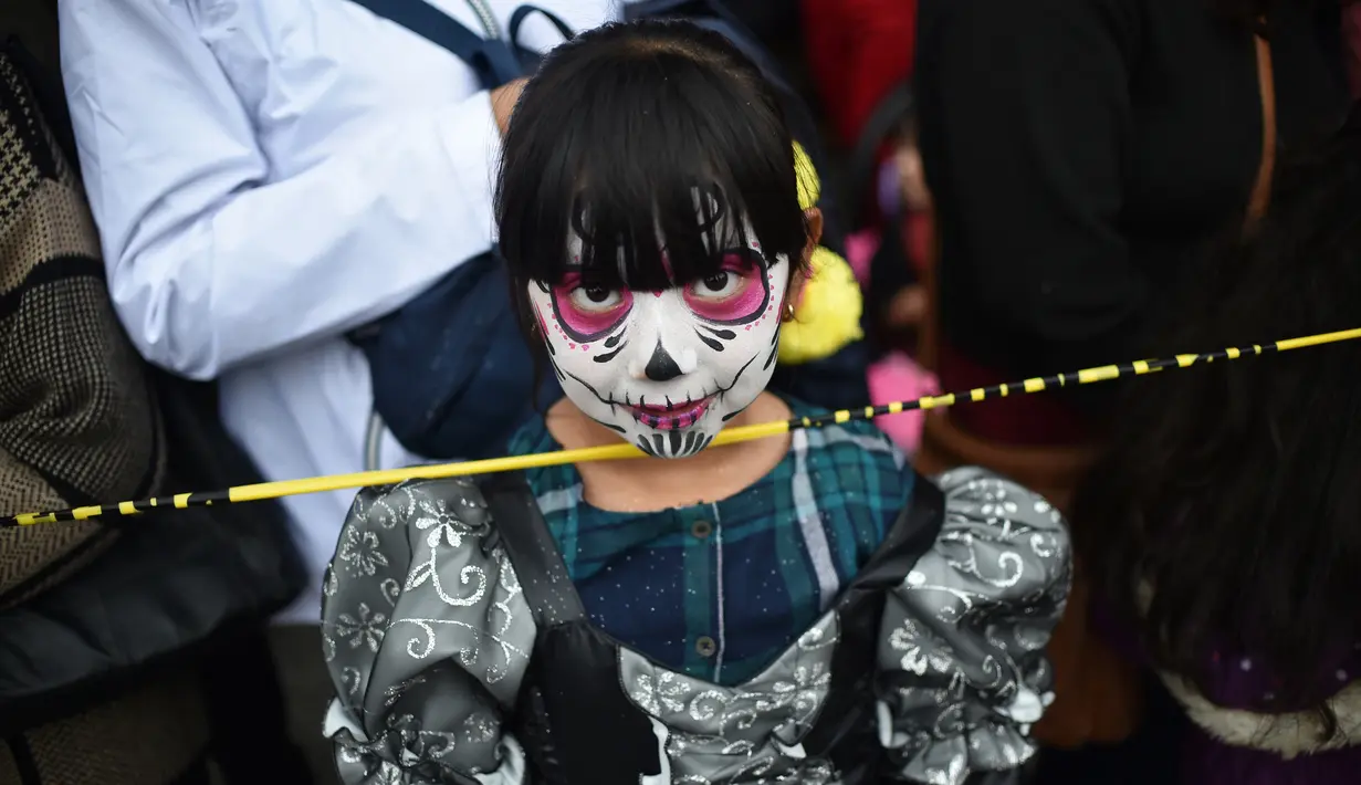 Seorang anak kecil berpakaian seperti "Catrina" ambil bagian dalam parade Hari Orang Mati di Reforma Avenue, Mexico City, 21 Oktober 2018. Banyak orang yang menggenakan kostum dan hiasan serba tongkorak yang memenuhi jalanan. (RODRIGO ARANGUA/AFP)