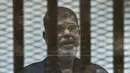 Mantan Presiden Mesir Mohammed Morsi berdiri di belakang jeruji besi saat menjalani sidang di Kairo, Mesir, 16 Juni 2015. Pria berusia 67 tahun tersebut meninggal saat menghadiri sesi pengadilan atas tuduhan spionase. (Khaled DESOUKI/AFP)