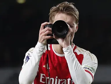 Pemain Arsenal, Martin Odegaard merayakan kemenangan dengan menjadi seorang fotografer setelah laga lanjutan Liga Inggris 2023/2024 melawan Liverpool di Emirates Stadium, London, Inggris, Minggu (05/02/2024) WIB. (AFP/Ian Kington)