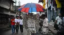 Seorang pedagang kaki lima menggunakan payung untuk melindungi anting-antingnya dari hujan di Kochi, negara bagian Kerala, India, Rabu (6/7/2022). Negara bagian selatan itu telah mewajibkan penggunaan masker di tempat-tempat umum menyusul meningkatnya kasus COVID-19. (AP Photo/ RS Iyer)