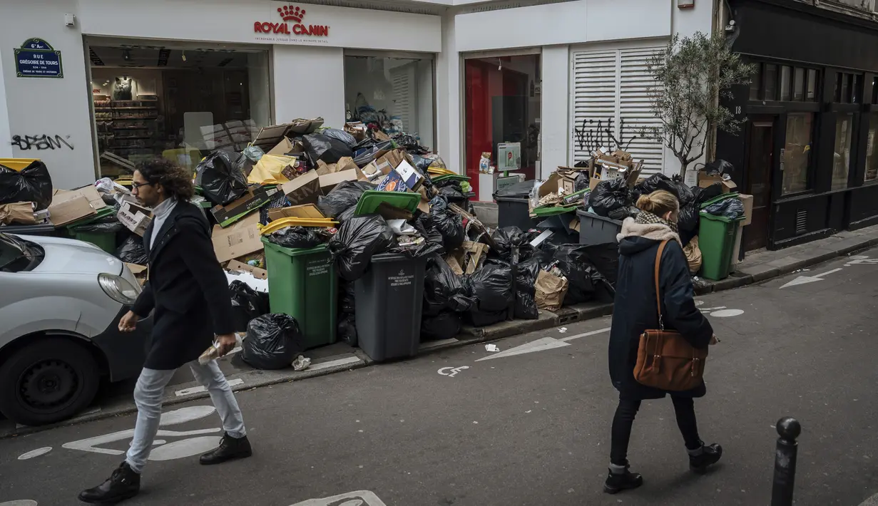 Pengguna jalan melintas di depan tumpukan sampah yang tidak diambil di Paris, Senin (13/3/2023). Sampah rumah tangga pun menumpuk di jalanan Sampah rumah tangga menumpuk di jalanan kota Paris, Prancis, Minggu (12/3/2023).  Sampah rumah tangga pun menumpuk di jalanan setelah pekerja pengangkut sampah melakukan pemogokan. (AP Photo/Lewis Joly)