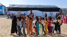 Guru-guru Palestina membariskan murid-murid di halaman sekolah yang didirikan oleh Asosiasi Kebudayaan Mayasem dengan dukungan UNICEF, sebelum pelajaran di kamp pengungsian di kawasan al-Qarara, Khan Yunis, di bagian selatan Jalur Gaza pada Selasa 7 Oktober 2025. (Omar AL-QATTAA/AFP)