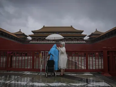 Pengunjung yang ditutupi jas hujan dan payung berdiri di gerbang masuk Kota Terlarang yang tertutup saat hujan badai membasahi Beijing, China, Minggu (30/7/2023). (AP Photo/Andy Wong)