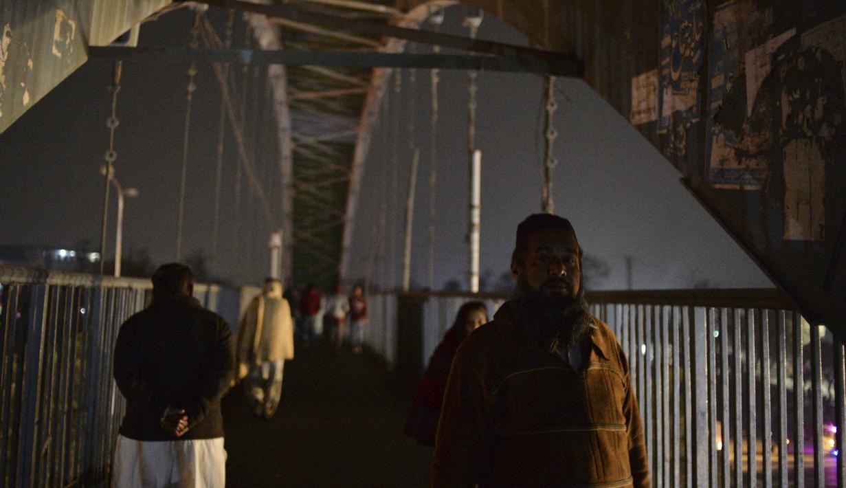 Orang-orang berjalan melintasi jembatan selama pemadaman listrik nasional, di Islamabad, Pakistan  pada 23 Januari 2023. Sebelumnya, Pakistan pernah mengalami pemadaman serupa pada Oktober tahun lalu. Butuh beberapa jam sebelum akhirnya listrik kembali pulih. (Farooq NAEEM / AFP)