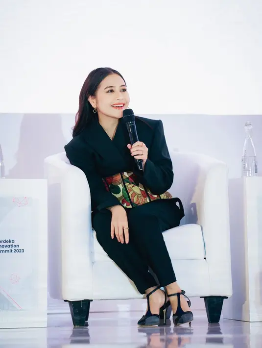 Di foto ini terlihat Prilly Latuconsina juga sedang menjadi pembicara di atas panggung. Ia memadukan blazer dan celana panjang hitam dengan obi bermotif abstrak dan bernuansa oranye yang menonjol. [Foto: Instagram/prillylatuconsina96]