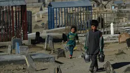 Afghan Zilgai (9) berjalan bersama adiknya, Khushnuma (4), ketika mencari pelanggan di pemakaman Kart-e-Sakhi, Kabul, 20 Februari 2016. Afghan setiap hari menjual air kepada para peziarah dengan penghasilan 1,5 USD/hari. (AFP PHOTO/Wakil KOHSAR)