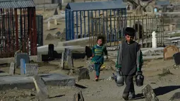 Afghan Zilgai (9) berjalan bersama adiknya, Khushnuma (4), ketika mencari pelanggan di pemakaman Kart-e-Sakhi, Kabul, 20 Februari 2016. Afghan setiap hari menjual air kepada para peziarah dengan penghasilan 1,5 USD/hari. (AFP PHOTO/Wakil KOHSAR)