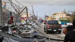 Sebuah mobil melaju melewati lingkungan yang hancur akibat Badai Melissa di Black River, Jamaika, pada 29 Oktober 2025. Badai Melissa menyebabkan kerusakan parah pada infrastruktur jalan raya, jaringan komunikasi, dan jaringan listrik, membuat sebagian besar wilayah mengalami pemadaman listrik. (Ricardo MAKYN/AFP)