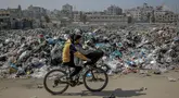 Anak-anak Palestina mengayuh sepeda melewati tempat pembuangan sampah besar di sepanjang jalan utama di Kota Gaza pada 24 Februari 2024. (Foto oleh AFP)