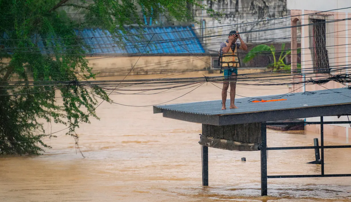 Diketahui, Thailand secara rutin mencatat bahwa hujan lebat biasanya terjadi sejak Juni hingga September. Tampak dalam foto, seorang pria bereaksi saat berdiri di atas atap di samping banjir bandang yang tinggi di Hat Yai, Provinsi Songkhla, Thailand selatan, pada 26 November 2025. (Arnun Chonmahatrakool/THAI NEWS PIX/AFP)