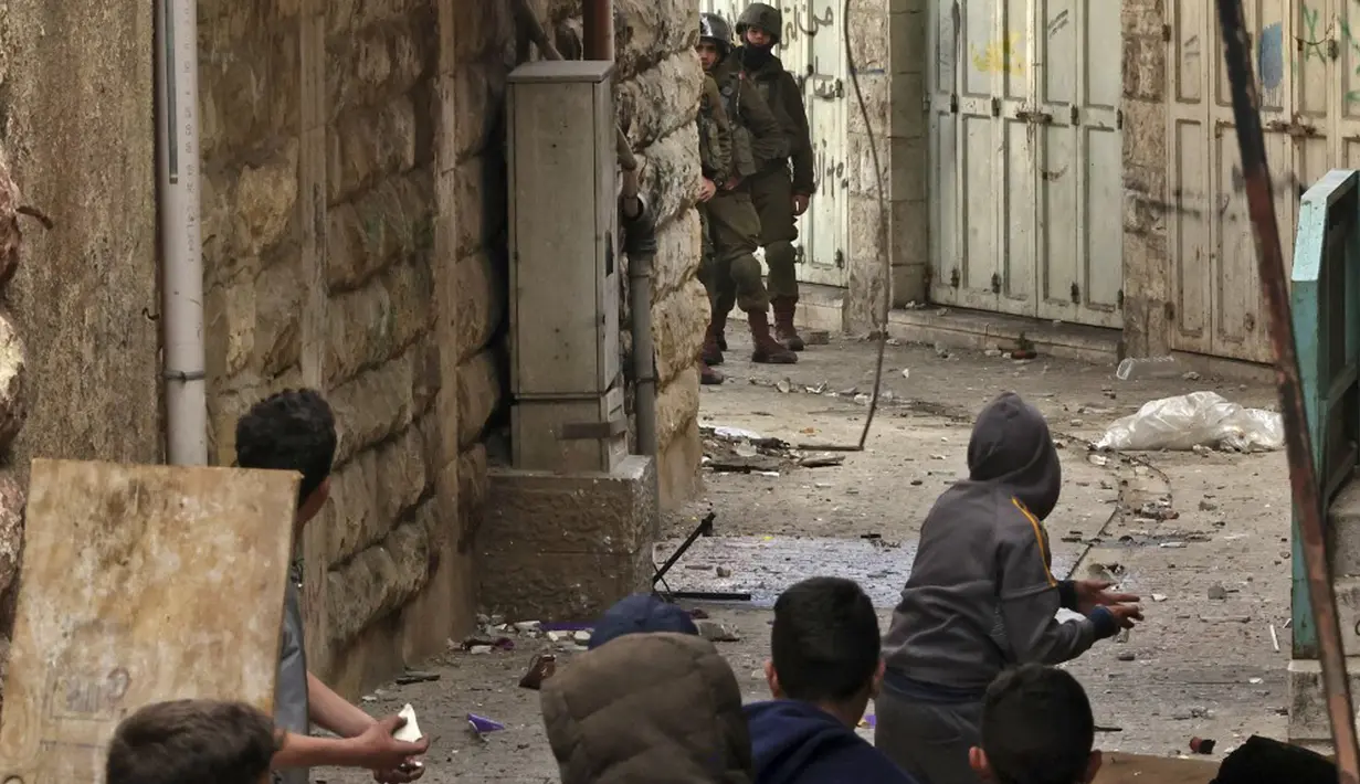 Tentara Israel berlindung sementara pengunjuk rasa Palestina bersiap untuk melempar batu saat bentrokan di pusat Kota Hebron, Tepi Barat, 4 Maret 2022. (HAZEM BADER/AFP)