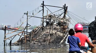 Pengendara sepeda motor melintas dekat kapal yang ludes dilalap api di Pelabuhan Muara Baru, Jakarta, Minggu (24/2). Sebanyak 18 unit kapal tradisional hangus akibat kebakaran pada Sabtu, 23 Februari 2019. (Merdeka.com/Iqbal Nugroho)