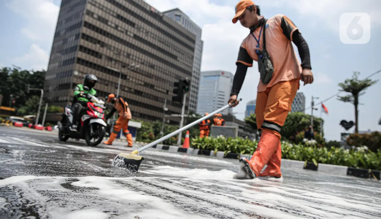 Pengendara motor berkendara dengan hati-hati saat anggota Penanganan Prasarana dan Sarana Umum (PPSU) membersihkan tumpahan oli di kawasan Jalan Thamrin, Jakarta, Selasa (4/10/2022). Pembersihan ceceran tumpahan oli tersebut agar pengendara motor tidak terjatuh. (Liputan6.com/Faizal Fanani)