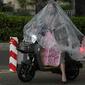 Seorang wanita bermasker menggunakan plastik besar untuk menutupi tubuhnya saat hujan di Beijing (24/5/2022). Beijing memperpanjang perintah bagi pekerja dan pelajar untuk tinggal di rumah dan memerintahkan pengujian massal tambahan pada Senin ketika kasus COVID-19 meningkat di ibu kota China. (AP Photo/Ng Han Guan)