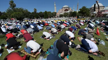 Umat Muslim berdoa saat menunaikan salat Jumat dengan latar belakang situs bersejarah Hagia Sophia di distrik bersejarah Sultanahmet di Istanbul, Jumat (24/7/2020). Hari ini, Hagia Sophia menyambut umat Islam melaksanakan salat Jumat pertama dalam 86 tahun.(AP Photo/Yasin Akgul)