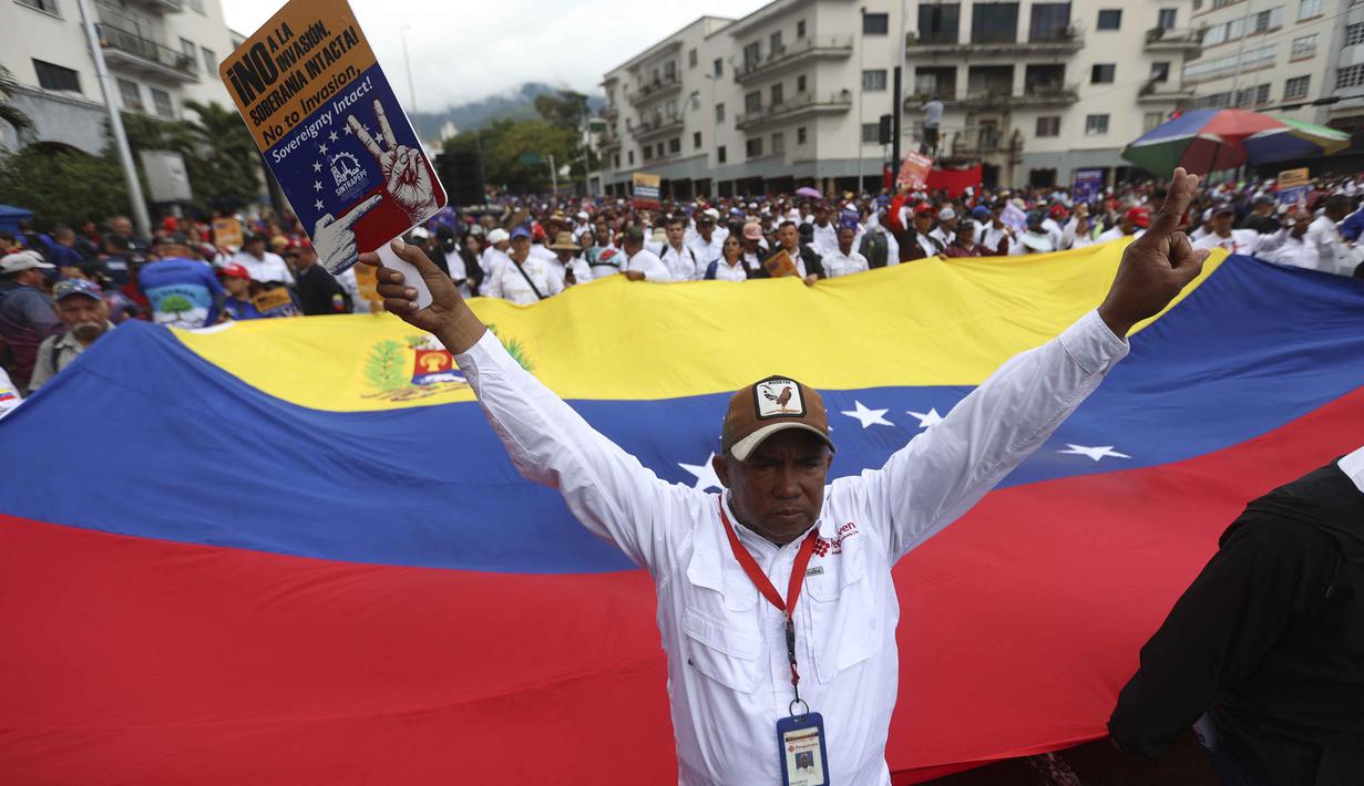 Massa yang berasal dari kelompok pekerja berunjuk rasa sambil mengibarkan bendera negara dan spanduk bertuliskan "Bebaskan Maduro". Tampak dalam foto, seorang demonstran mengacungkan tanda kemenangan di depan bendera nasional Venezuela yang besar selama pawai dukungan untuk mantan Presiden Venezuela Nicolas Maduro dalam unjuk rasa yang diselenggarakan oleh para pekerja di Caracas pada 14 Januari 2026. (Pedro MATTEY/AFP)