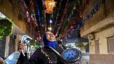 Dalal, seorang wanita Mesir yang dikenal sebagai 'musaharati', berjalan di sepanjang jalan sambil memukul gendang dan menyerukan umat Muslim untuk bangun dan makan sahur selama bulan suci Ramadan di distrik Hadayek el-Maadi, selatan Kairo pada Minggu 1 Maret 2026. Musaharati merupakan tradisi kuno Ramadan di negara-negara Arab, Palestina, Mesir, dan lainnya. (Khaled DESOUKI/AFP)