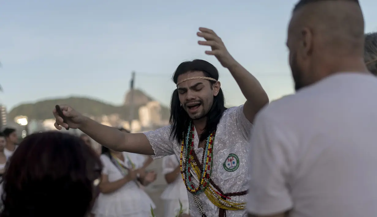 Seorang penganut kepercayaan Afro-Brasil bernyanyi saat memberikan persembahan untuk Yemenja sang Dewi Laut, ketika menyambut tahun baru di Pantai Copacabana di Rio de Janeiro (29/12/2019). (AFP/Mauro Pimentel)