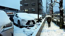 Seorang warga berjalan di antara mobil-mobil yang tertutup salju di Tokyo, Jepang, Senin (18/1). Akibat banyaknya tumpukan salju yang menyelimuti daerah metropolitan Tokyo, moda transportasi massa pun lumpuh. (AFP PHOTO/Yoshikazu Tsuno)