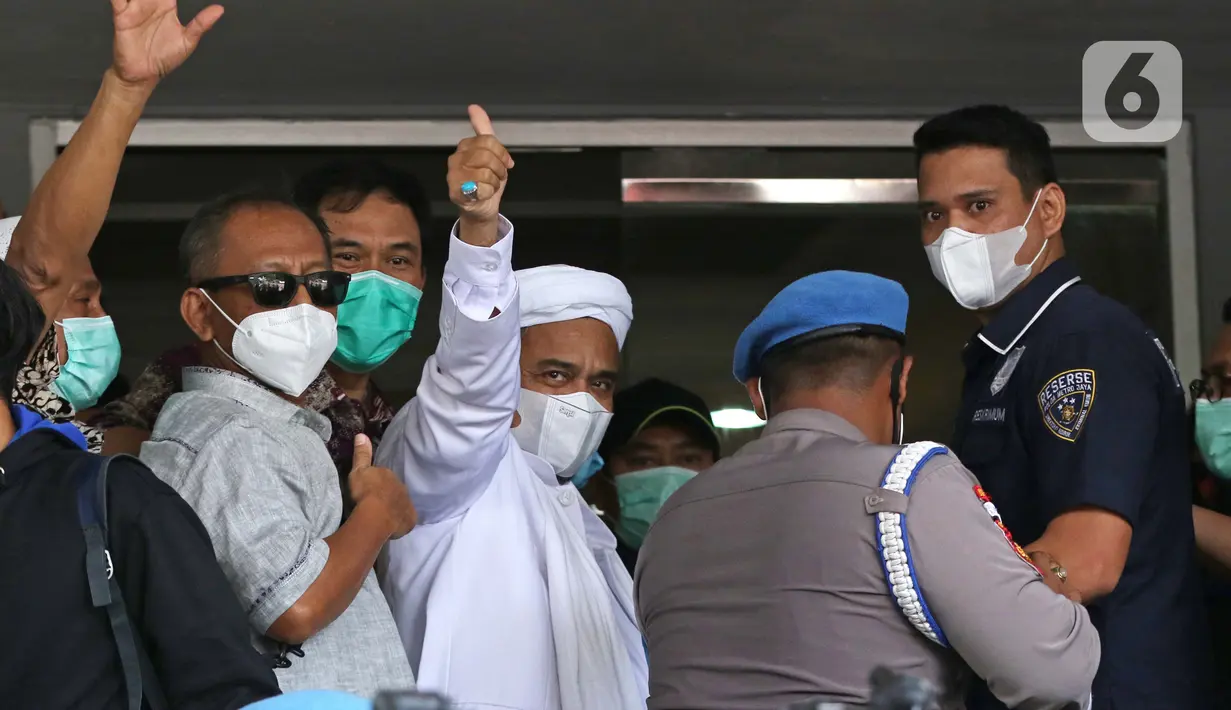 Rizieq Shihab (tengah) melambaikan tangan sesaat sebelum masuk gedung utama Mapolda Metro Jaya, Jakarta, Sabtu (12/12/2020). Rizieq Shihab akan menjalani pemeriksan sebagai tersangka penghasutan dan kerumunan di tengah pandemi Covid-19. (Liputan6.com/Helmi Fithriansyah)