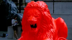 Wanita bermain ponsel di dekat singa fluorescent merah di London (19/9). Masyarakat dapat mengirimkan kata-kata, yang kemudian singa mengaum sebagai puisi, dan teks puitis dan diproyeksikan ke singa lainnya dan Kolom Nelson. (AP Photo/Frank Augstein)