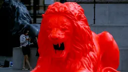 Wanita bermain ponsel di dekat singa fluorescent merah di London (19/9). Masyarakat dapat mengirimkan kata-kata, yang kemudian singa mengaum sebagai puisi, dan teks puitis dan diproyeksikan ke singa lainnya dan Kolom Nelson. (AP Photo/Frank Augstein)