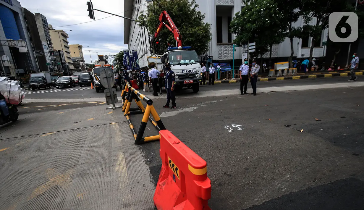 Petugas Dinas Perhubungan DKI Jakarta menurunkan beton barrier saat penutupan akses jalan menuju kawasan Kota Tua, Jumat (18/12/2020). Pemprov DKI membatasi moda transportasi melintasi kawasan wisata Kota Tua seiring penerapan kawasan rendah emisi atau Low Emission Zone. (Liputan6.com/Johan Tallo)