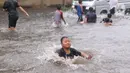 Sejumlah anak bermain banjir saat melanda jalan Bayangkara Pusdiklat, Kota Tangerang Selatan, Banten, Selasa (2/11/2021). Aksi anak anak tersebut dapat membahayakan keselamatan jiwa karena banyaknya kendaraan yang melintas menerjang banjir. (Liputan6.com/Angga Yuniar)
