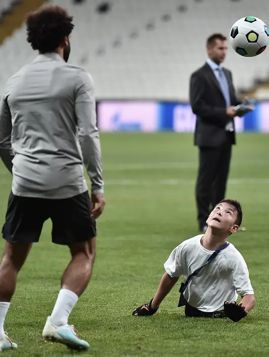 Seorang anak tanpa memiliki kaki menyundul bola saat bermain dengan gelandang Liverpool, Mohamed Salah saat sesi pelatihan jelang bertanding melawan Chelsea pada Piala Super Eropa 2019 di Stadion Taman Besiktas, di Istanbul (13/8/2019). (AFP Photo/Ozan Kose)