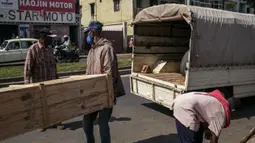 Tukang kayu memasukkan peti mati yang telah dipesan ke mobil di jalan raya umum, di Antananarivo, Madagaskar, Rabu (14/4/2021). Selama tiga minggu terakhir, Pak Jean dan timnya memproduksi antara 15 hingga 20 peti mati per hari, padahal sebelumnya hanya 3 atau 4 peti mati per hari. (RIJASOLO/AFP)