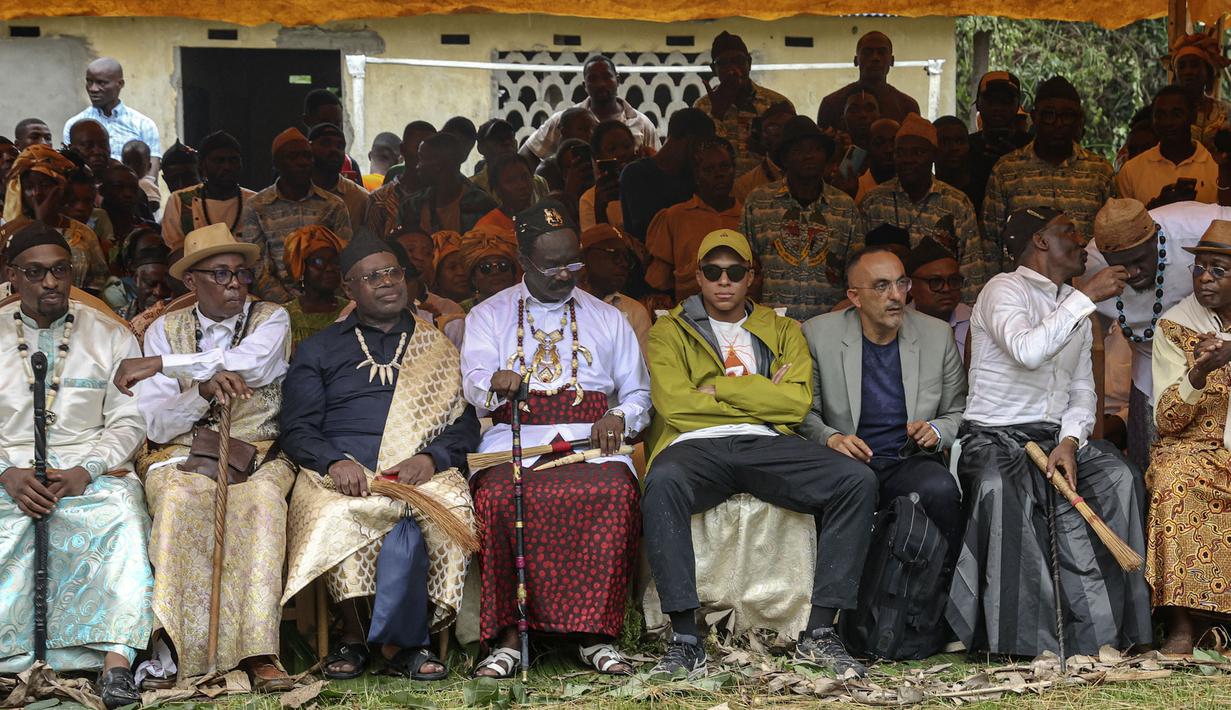 Pemain Paris Saint-Germain dan kapten Timnas Prancis, Kylian Mbappe (keempat kanan) duduk bersama kepala desa dan tokoh-tokoh saat upacara tradisional ketika dirinya mengunjungi desa ayahnya, Wilfrid Mbappe, di Djebale pada 8 Juli 2023. (AFP/Daniel Beloumou Olomo)