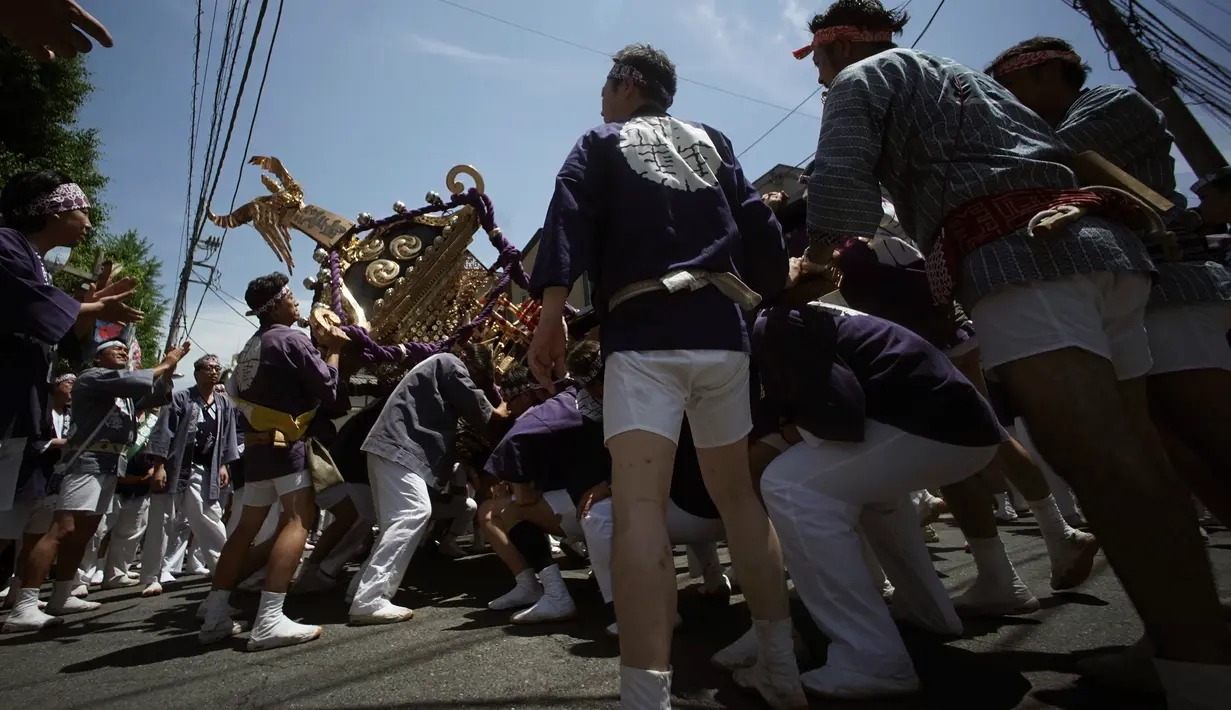 Puluhan peserta berusaha mengangkat Mikoshi saat festival Tenno-sai di Kuil Susanoo di Tokyo, Jepang (3/6). Dalam ritual ini, selain upacara di kuil Shinto, mereka juga membawa mikoshi ke jalan-jalan sekitar. (AP Photo / Eugene Hoshiko)
